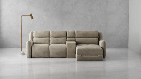 A modern beige sectional sofa with a right-facing chaise lounge, set against a minimalist gray concrete wall and floor with a minimalist floor lamp on the left.