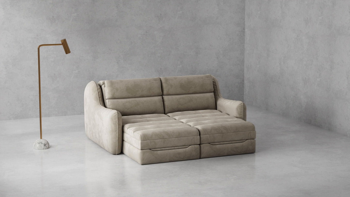 A modern beige upholstered sofa with a chaise lounge section, set in a minimalist concrete room next to a slim floor lamp.