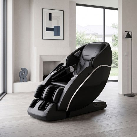 A modern black massage chair with silver trim, positioned in a contemporary minimalist living room with light wood floors, a fireplace, and large windows.