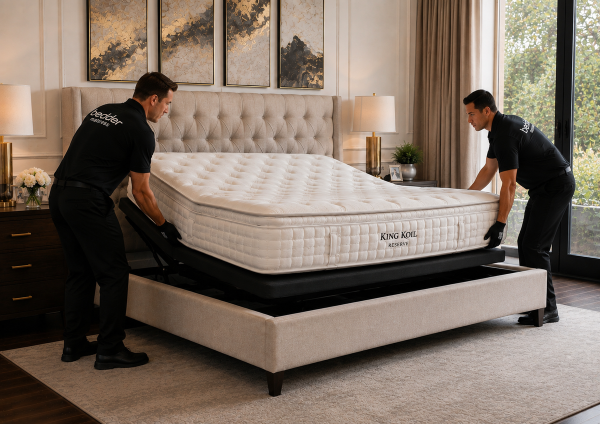 Professional Setup. The mattress already inside the bedroom with two delivery professionals carefully positioning/installing it on an adjustable base inside a finished bed.
