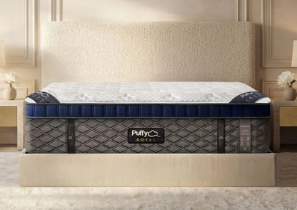 A Puffy Royal mattress shown on a bed in a styled bedroom setting. The mattress features a white quilted top, a navy blue side bolster, and a dark gray quilted base with the Puffy Royal logo on the front.